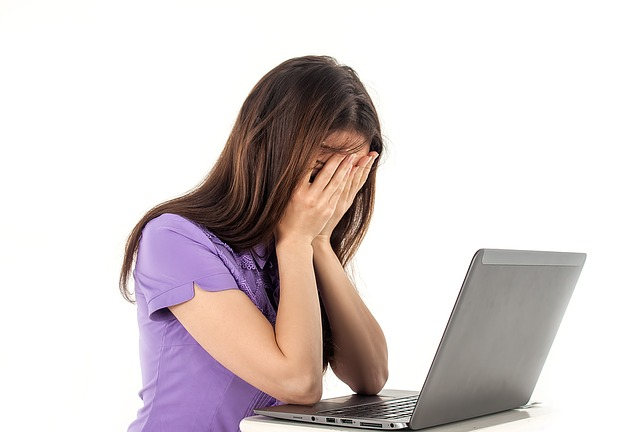 パソコンの前で顔を手で覆い落胆する女性